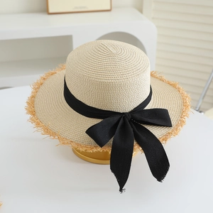 Detail of raffia straw hat with frayed edges and a black ribbon bow for sun protection