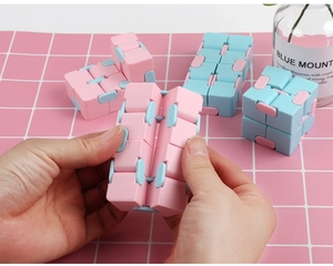 Pink and blue infinity cube stress relief toy demonstrated by hand on grid background