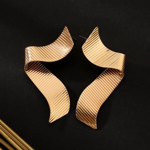 Macro detail of golden wave earrings with elegant vertical stripe texture on a black background
