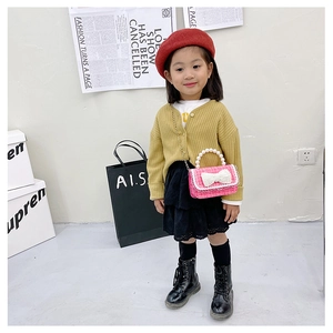 Detailed view of pink tweed kids crossbody bag with pearl handle and bow worn by a model