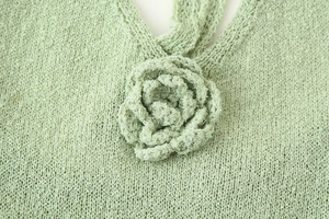 Detail shot of green knit dress showing textured fabric and 3D floral accent