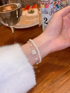 Detalle de la pulsera de doble capa con perlas, dije de camelia blanca y cadena de oro