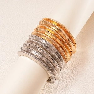 Detail of stacked gold and silver textured coil bracelets on a white display stand