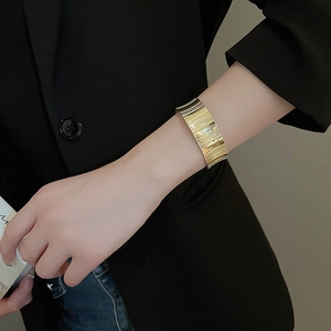 Close-up of a wide golden wavy textured cuff bracelet worn on a female model's wrist