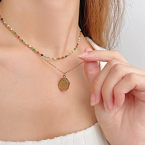 Détail d'un collier doré double épaisseur avec des perles colorées et un pendentif rose gravé
