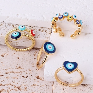 Detailed view of colorful Evil Eye rings on white stone displaying gold-plated enamel design
