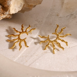Close-up of golden sunflower earrings on a textured stone base with artistic shadows