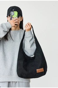 Detail of black corduroy shoulder bag with textured finish and brand label on a model