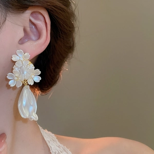 Détail de grandes boucles d'oreilles fleurs blanches avec gouttes de perles sur modèle