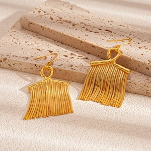 Close-up of golden tassel drop earrings on a natural stone background with metal texture