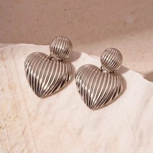 Detailed view of silver metal earrings with striped heart charms on a textured shell base