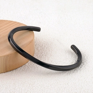 Detail of glossy black C-shape open cuff bracelet on white sand with wooden accents