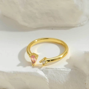 Detailed close-up of open ring with pink pear-cut zircon on gold-plated band