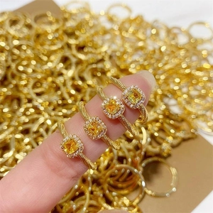 Hand wearing four square yellow crystal halo rings with vintage twisted gold plated bands