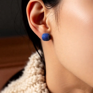 Close-up of blue zircon stud earring with beaded texture worn on model's ear