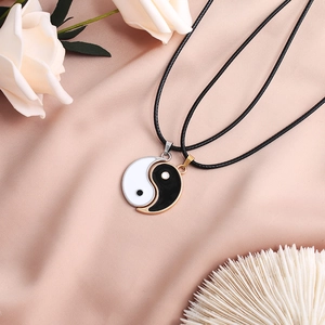 Yin Yang Tai Chi couple necklaces with black and white pendants on pink silk background