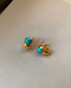 Detailed view of C-shaped 18k gold plated turquoise stud earrings with silicone backings