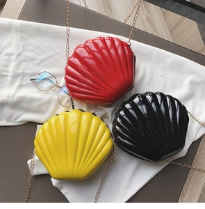 Detailed view of three shiny shell-shaped crossbody bags in red, yellow and black with chains