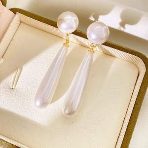 Detail of drop-shaped white pearl earrings with gold accents in a premium jewelry box