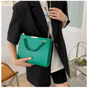 Detail of green crocodile texture handbag with gold chain strap shown on model