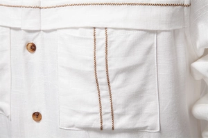Macro view of white linen shirt fabric featuring brown wood buttons and wave stitching