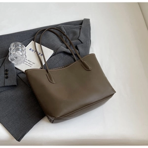 Detail shot of the large dark brown leather tote bag with a sleek grey blazer and book