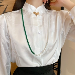 Detail of emerald and pearl beaded necklace styled on white traditional silk shirt