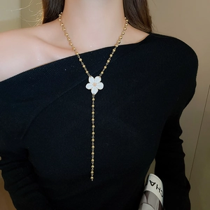 Close-up of a long golden Y-necklace with white flower pendant on a model in black