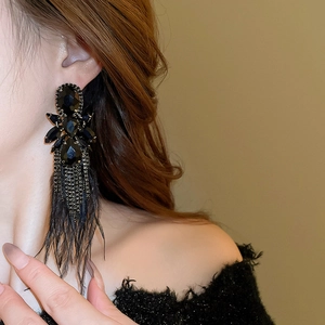 Close-up of long black feather tassel earrings with dark rhinestones on a model