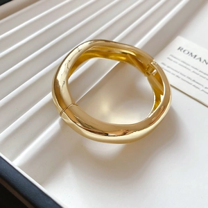Close-up of gold chunky organic wave bangle showing the metal hinge and glossy finish