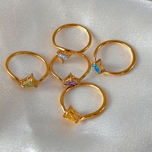 Detailed view of five colorful triangle zircon rings on elegant white silk fabric