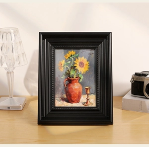 Close-up of vintage black embossed frame with sunflower oil painting on a wooden desk