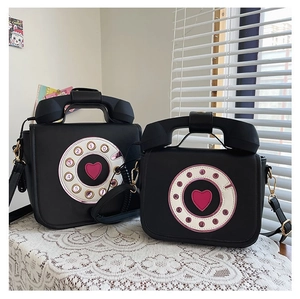 Close-up of two black retro telephone-shaped crossbody bags with pink heart dial details