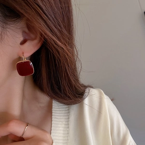 Close-up of geometric deep red enamel earrings and a minimalist slim gold ring