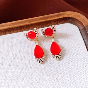 Detail of gold earrings with red oval and teardrop stones accented by crystals on fabric