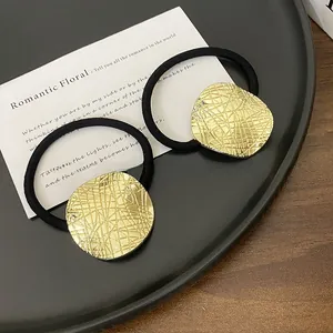 Detail of black elastic hair ties with textured gold metal geometric cubes on dark tray