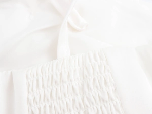 Close-up of white crop top featuring smocked fabric detail and elegant tie straps