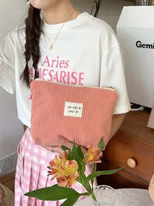 Pink corduroy makeup bag with beige label held by a model in a cozy indoor setting