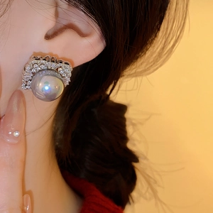 Detail showing a grey pearl earring with silver zircon setting on a female ear