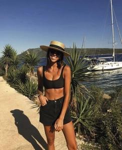 Flat top wheat straw hat with black ribbon shown in a scenic beach vacation setting