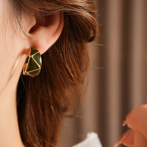 Macro shot of vintage gold C-shape earrings with green enamel texture on a model
