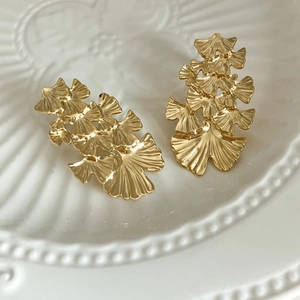 Close-up of stacked gold ginkgo leaf earrings on a white vintage ceramic plate
