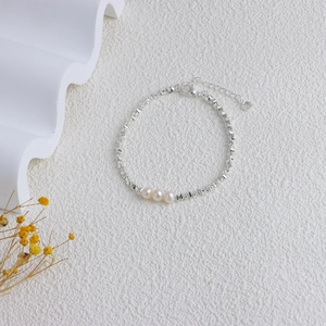Detail of silver chain bracelet with three white pearls on a textured background