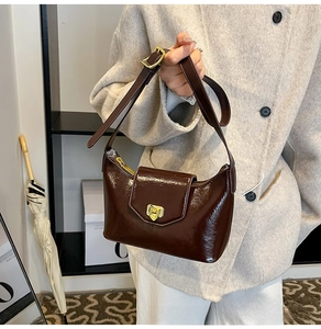 Detail of dark brown glossy leather crescent bag with golden twist lock on beige coat