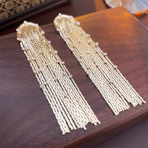 Detailed view of long gold tassel earrings with shimmering crystals on a wooden tray