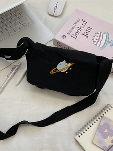 Black canvas crossbody messenger bag with colorful planet embroidery on a desk