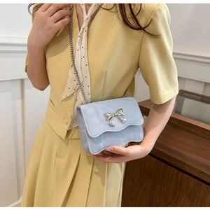Détail du sac à bandoulière bleu clair avec nœud argenté porté sur un tailleur jaune