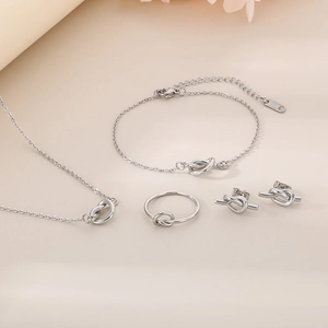 Silver knotted jewelry set including necklace, bracelet, ring and earrings on beige background