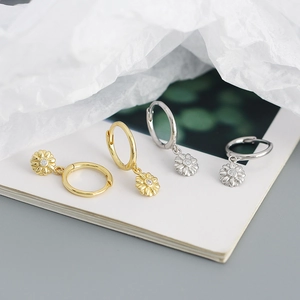 Detailed view of silver and gold daisy pendant hoop earrings on white paper