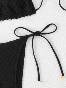 Detailed macro shot of black popcorn texture bikini fabric with shell bead side-tie detail